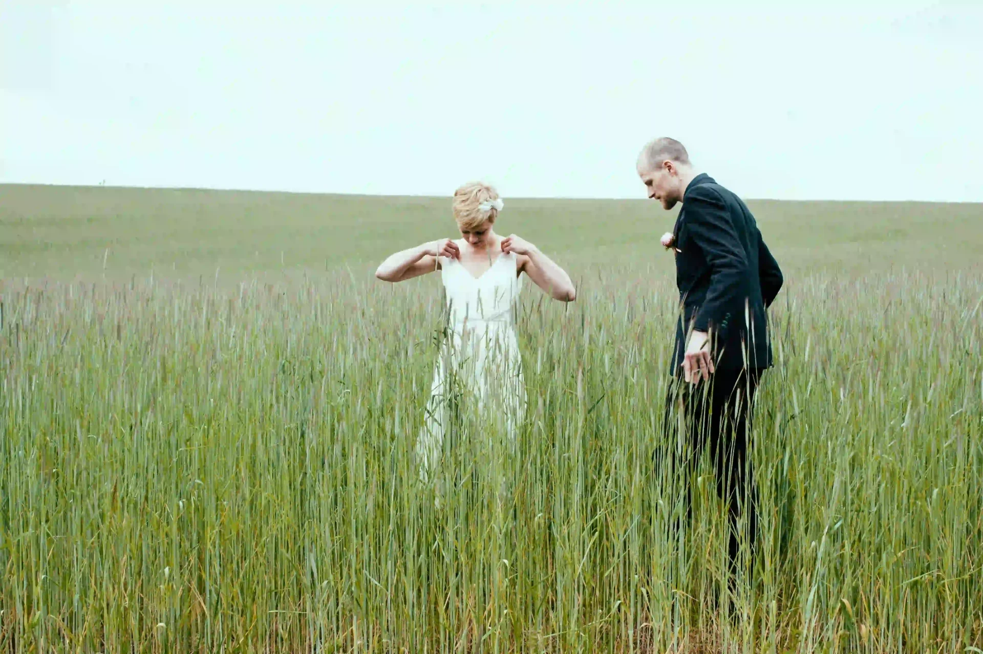 Bride adjusting her dress while the groom stands beside her in tall grass