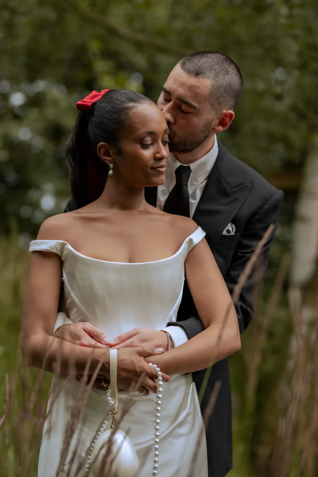 Groom kissing the bride on the forehead in a garden