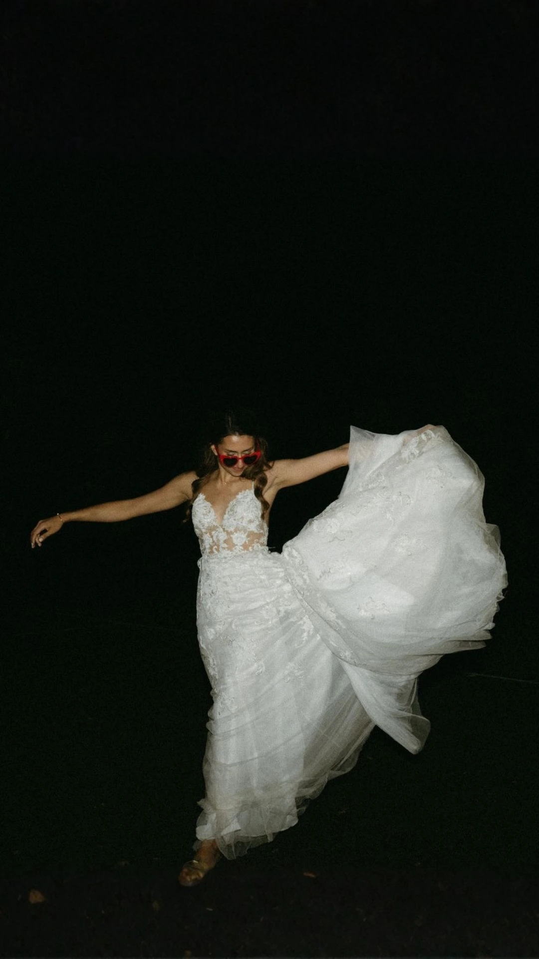 Bride lifting her wedding dress while dancing outdoors at night