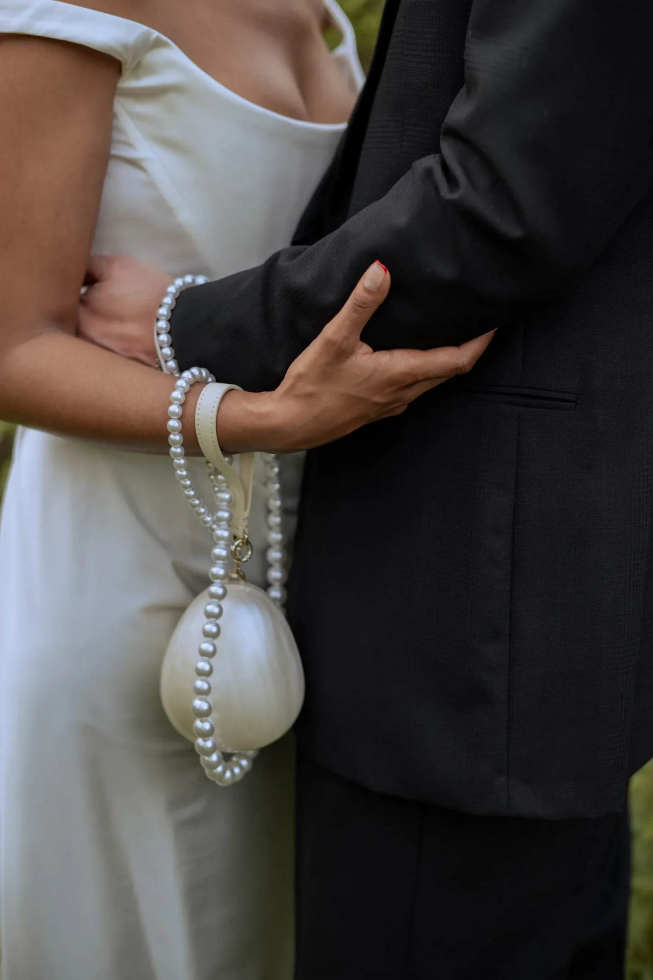 Close-up of a bride holding the groom's arm, with a pearl accessory