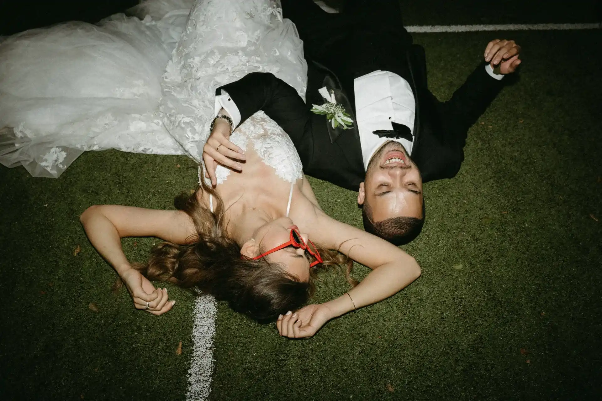 Bride and groom lying on the grass, the bride wearing red sunglasses