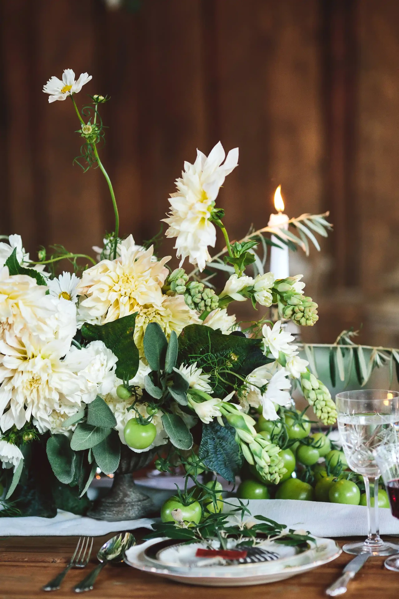 Wedding table with white flowers and candles in front of a weathered wooden wall