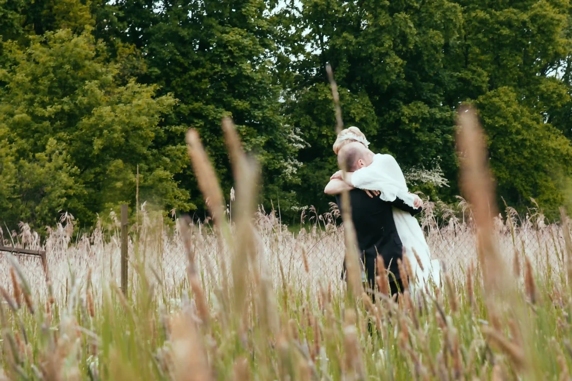 Bride and groom standing together in tall grass in a field