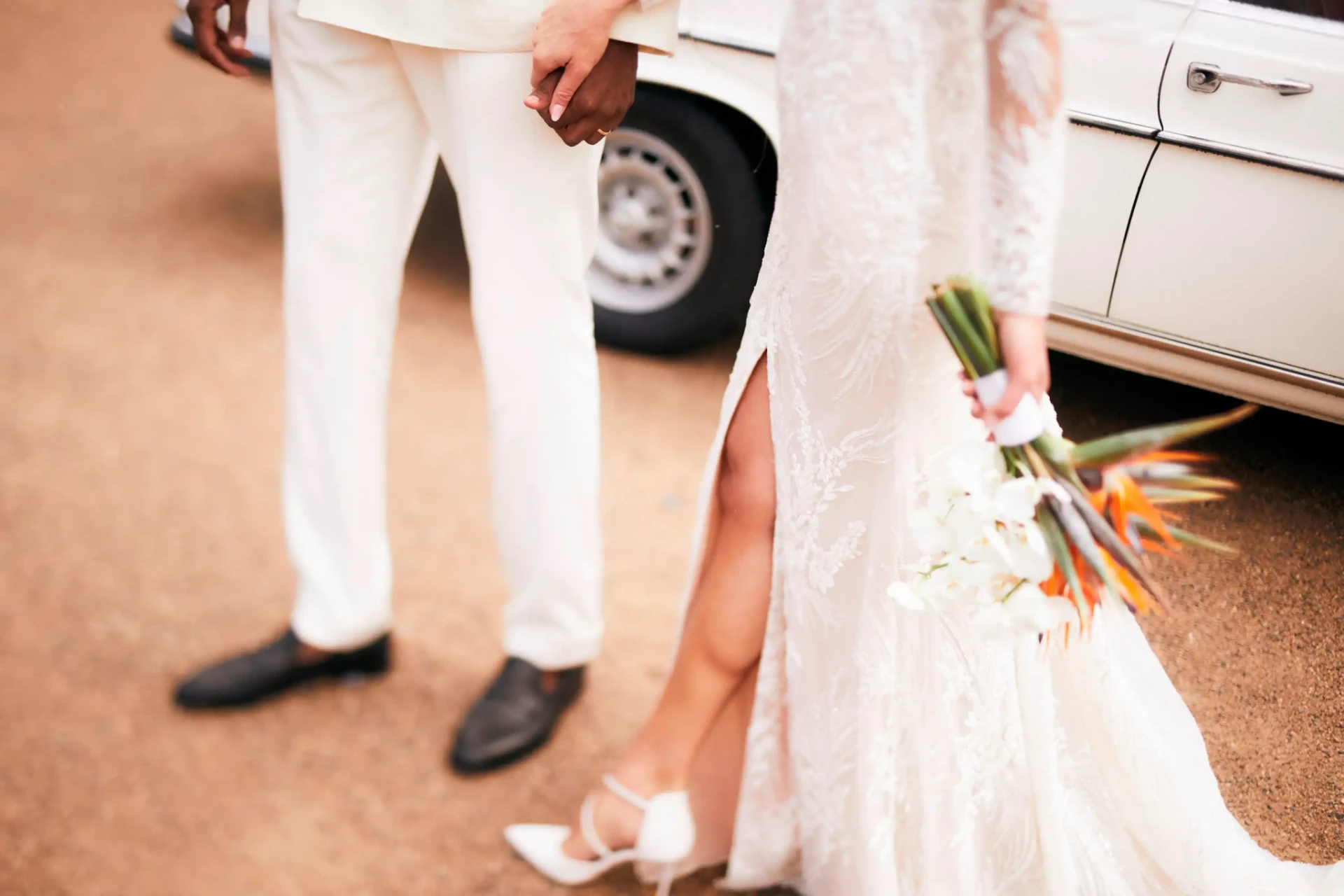 Close-up of the bride and groom beside a car, with the bride holding a bouquet