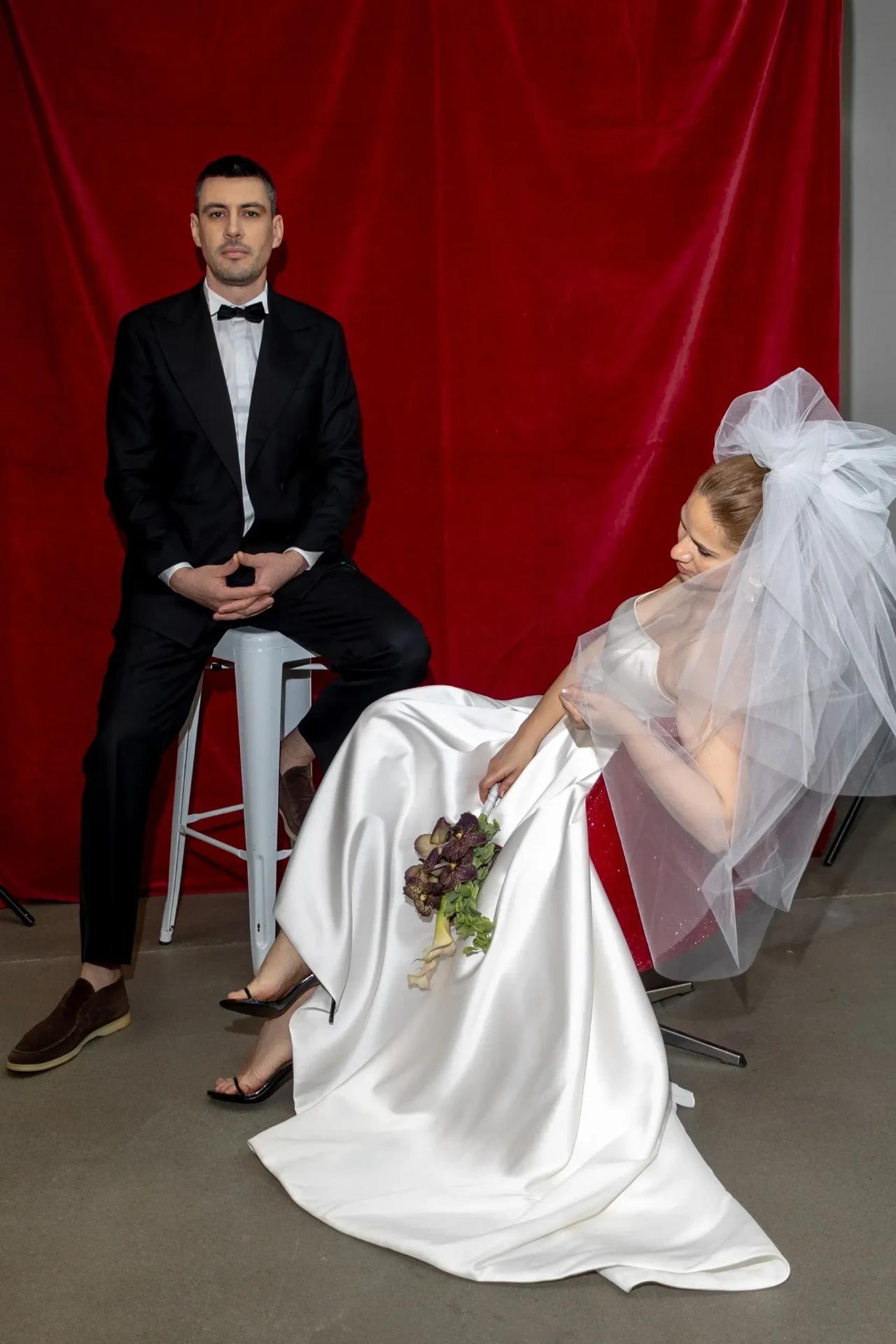 Wedding couple with a bouquet in front of a red backdrop