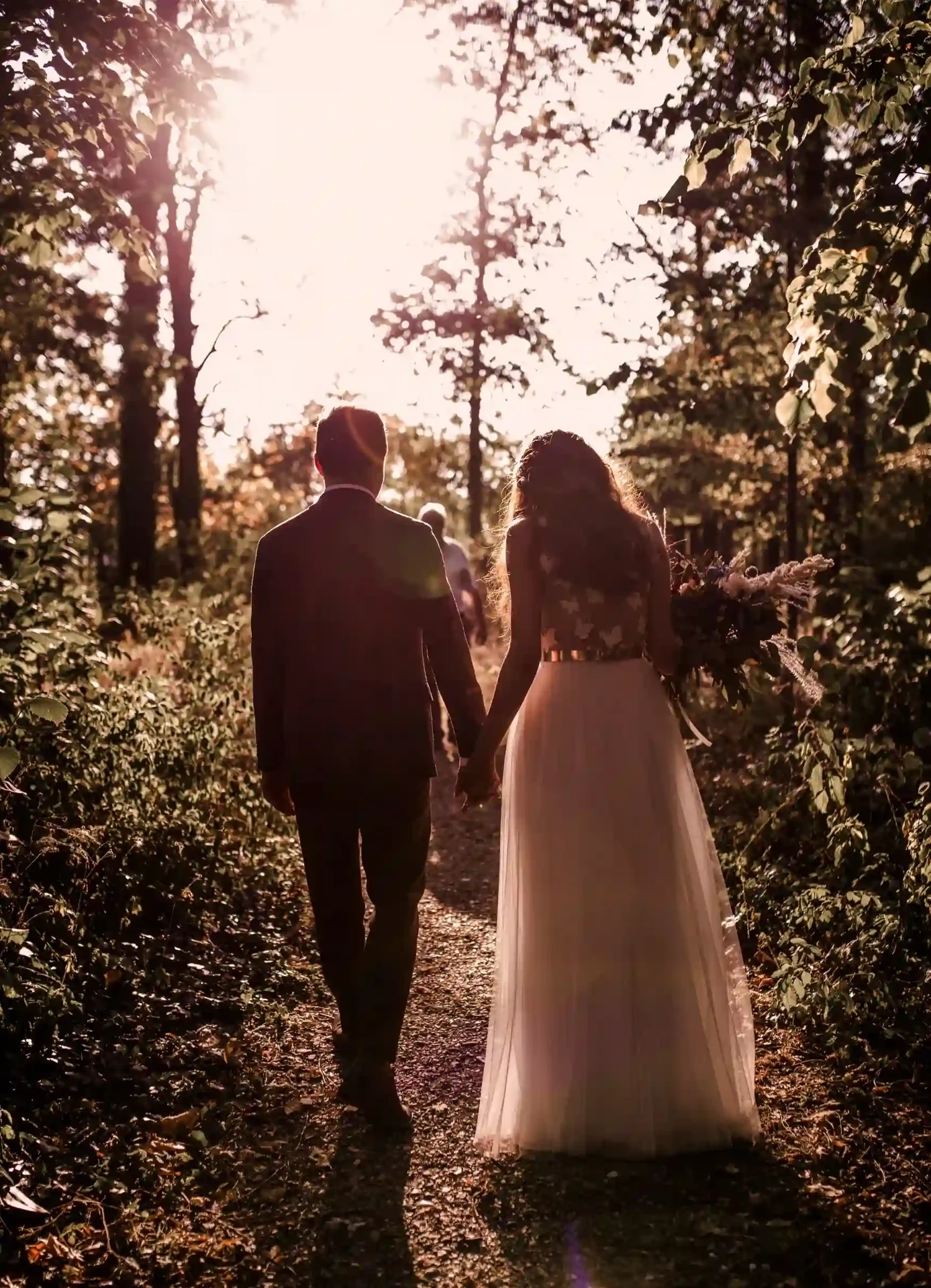 Bride and groom walking hand in hand through the garden in sunlight