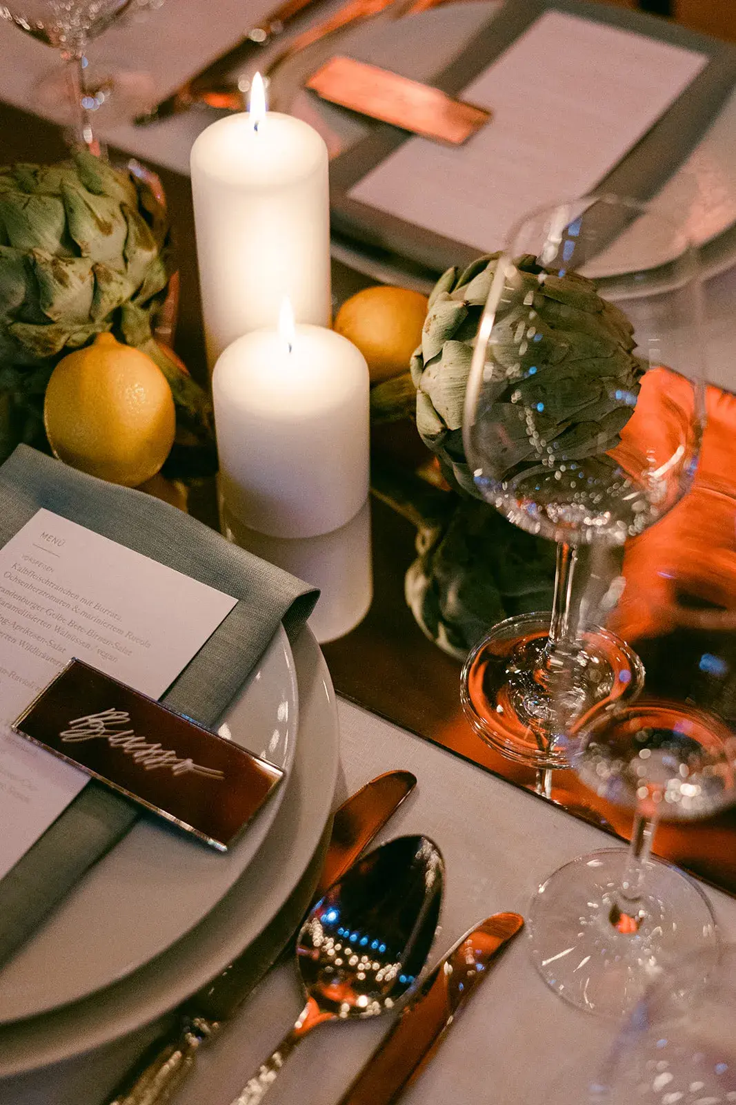 Festively set place with candles, artichokes, citrus fruit and glassware