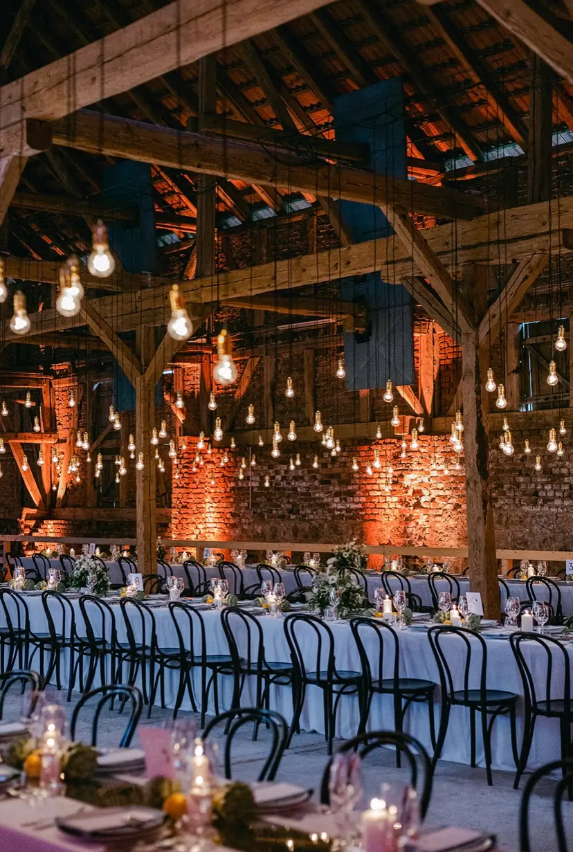 Wedding reception with long dining tables and hanging lights in a rustic barn