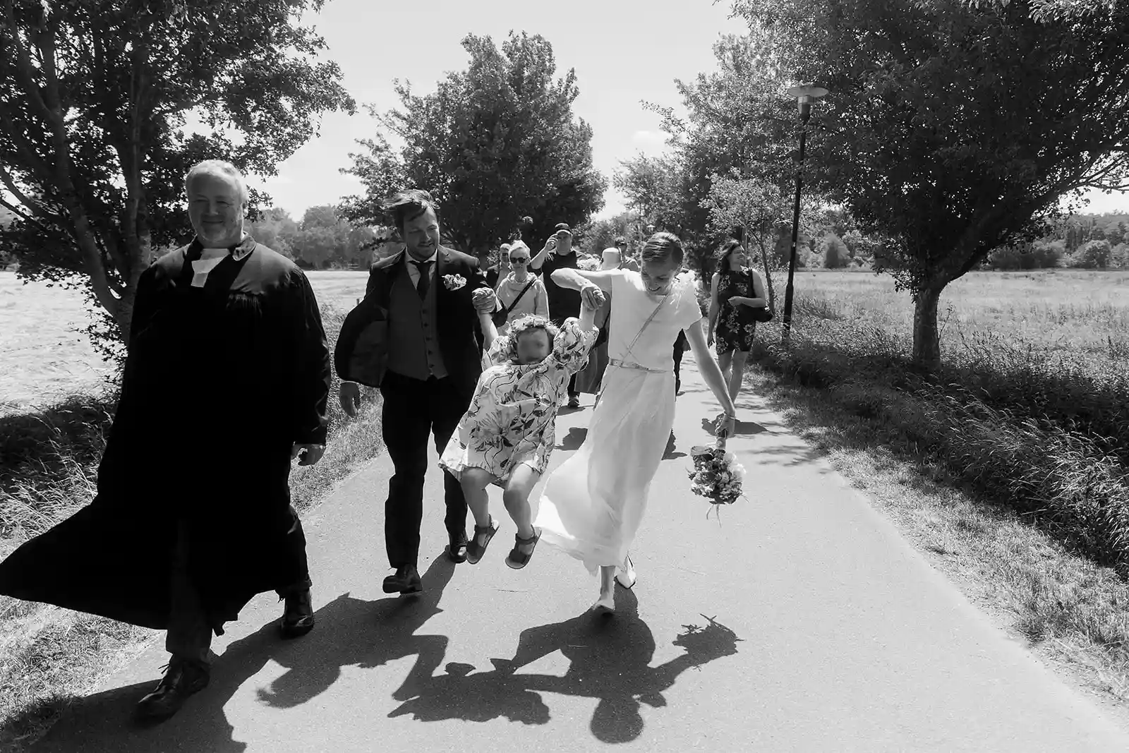 Black-and-white photograph of the wedding couple with guests on a path