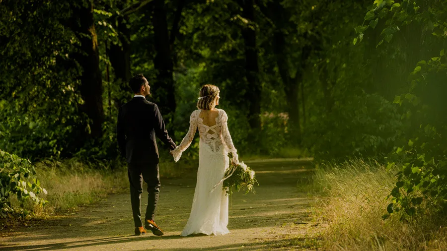 Bride and groom walking hand in hand along a green tree-lined path