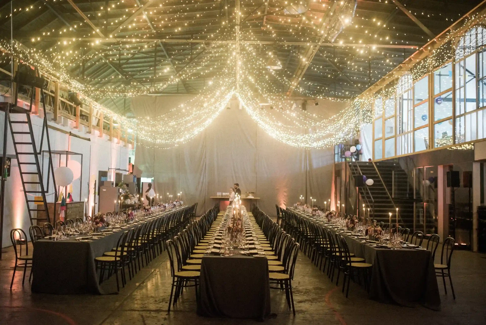 Long dinner table in a high-ceilinged hall with fabric installations and string lights
