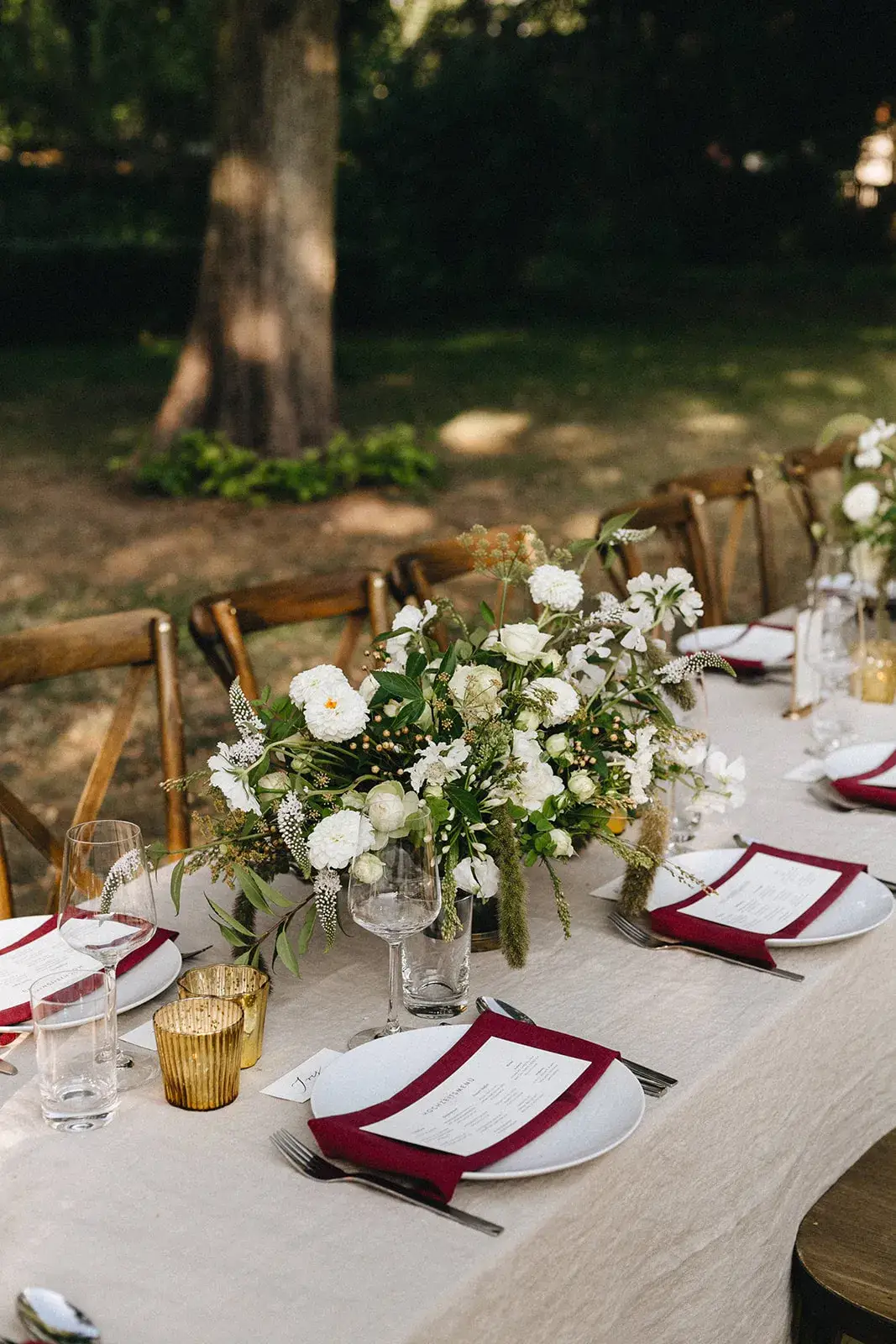 Lange, weiß gedeckte Tafel im Garten mit roten Servietten und weißen Blumen