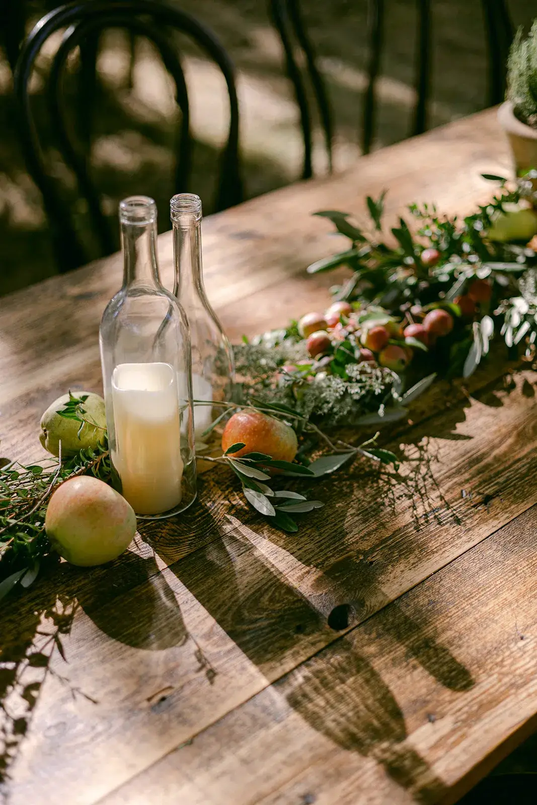 Wedding table detail with glass bottles, candles and green floral arrangements