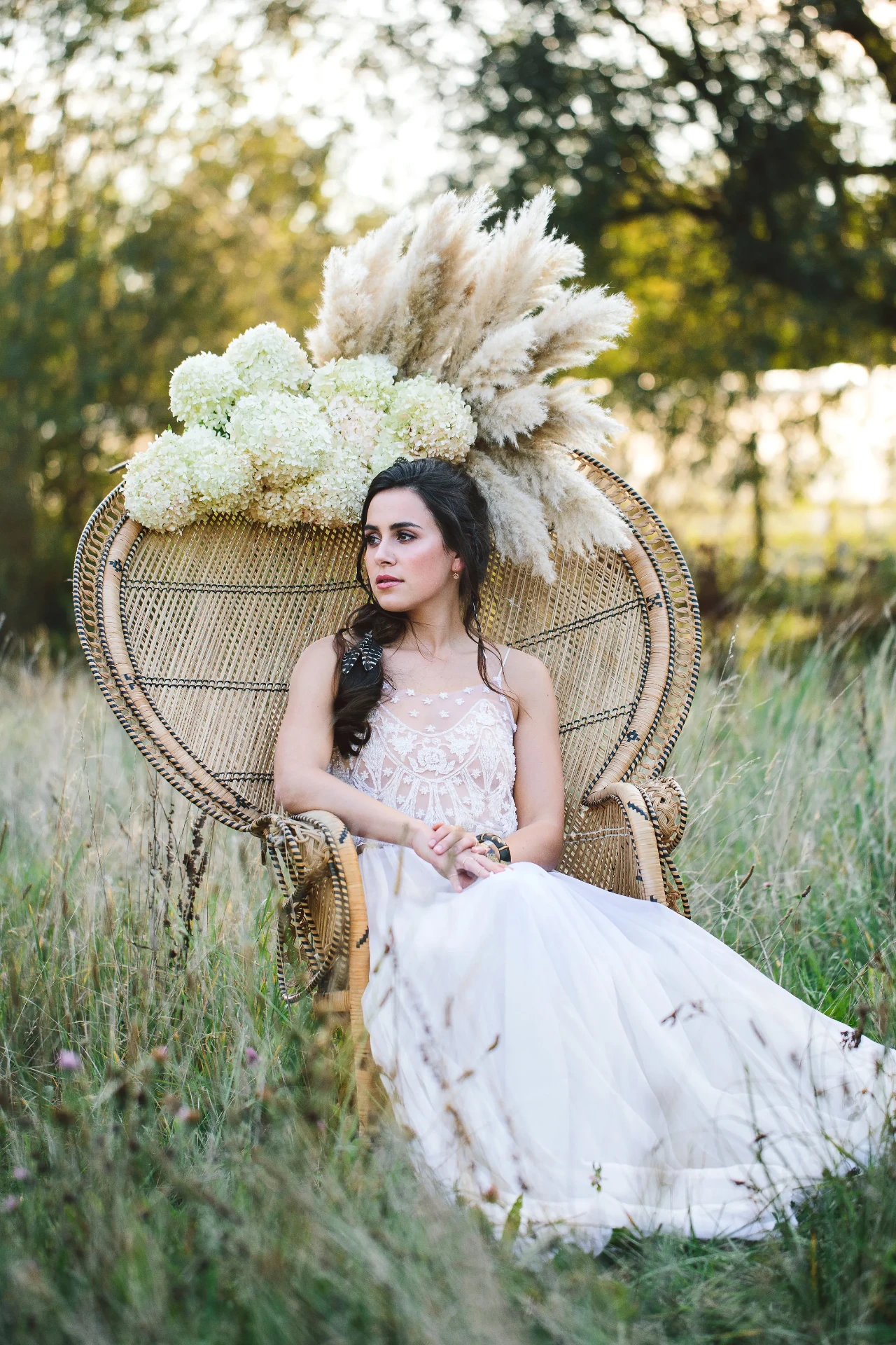 Bride seated in a round rattan chair with pale pampas grass and floral arrangements