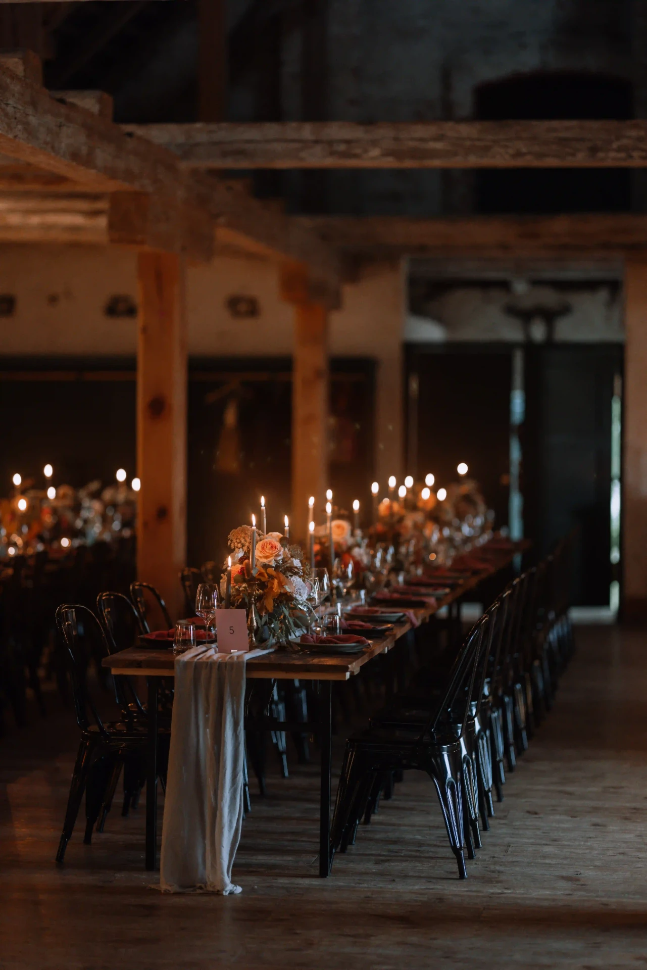 Long wedding table in a rustic barn illuminated by candlelight
