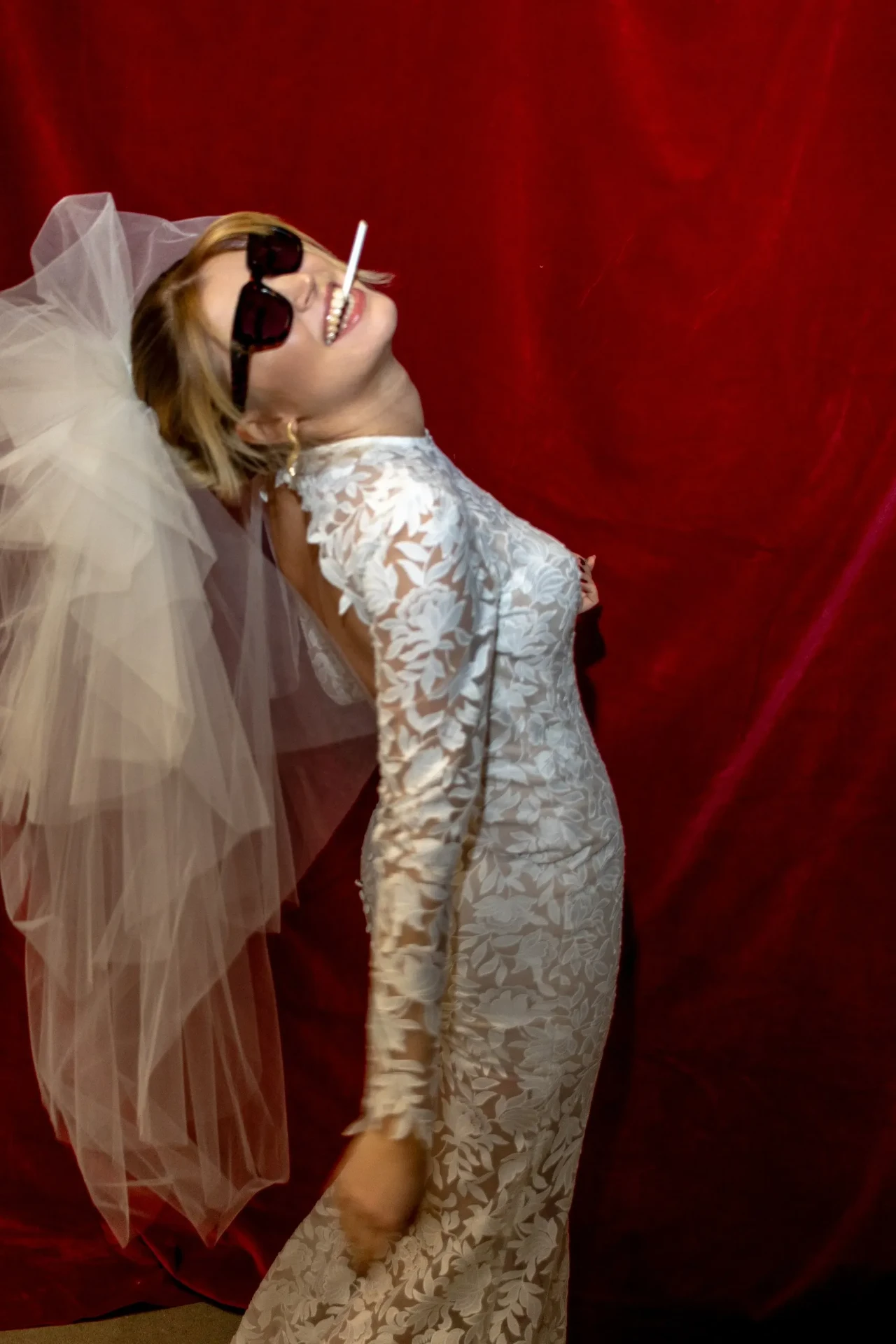 Bride in a lace wedding dress and sunglasses against a red backdrop