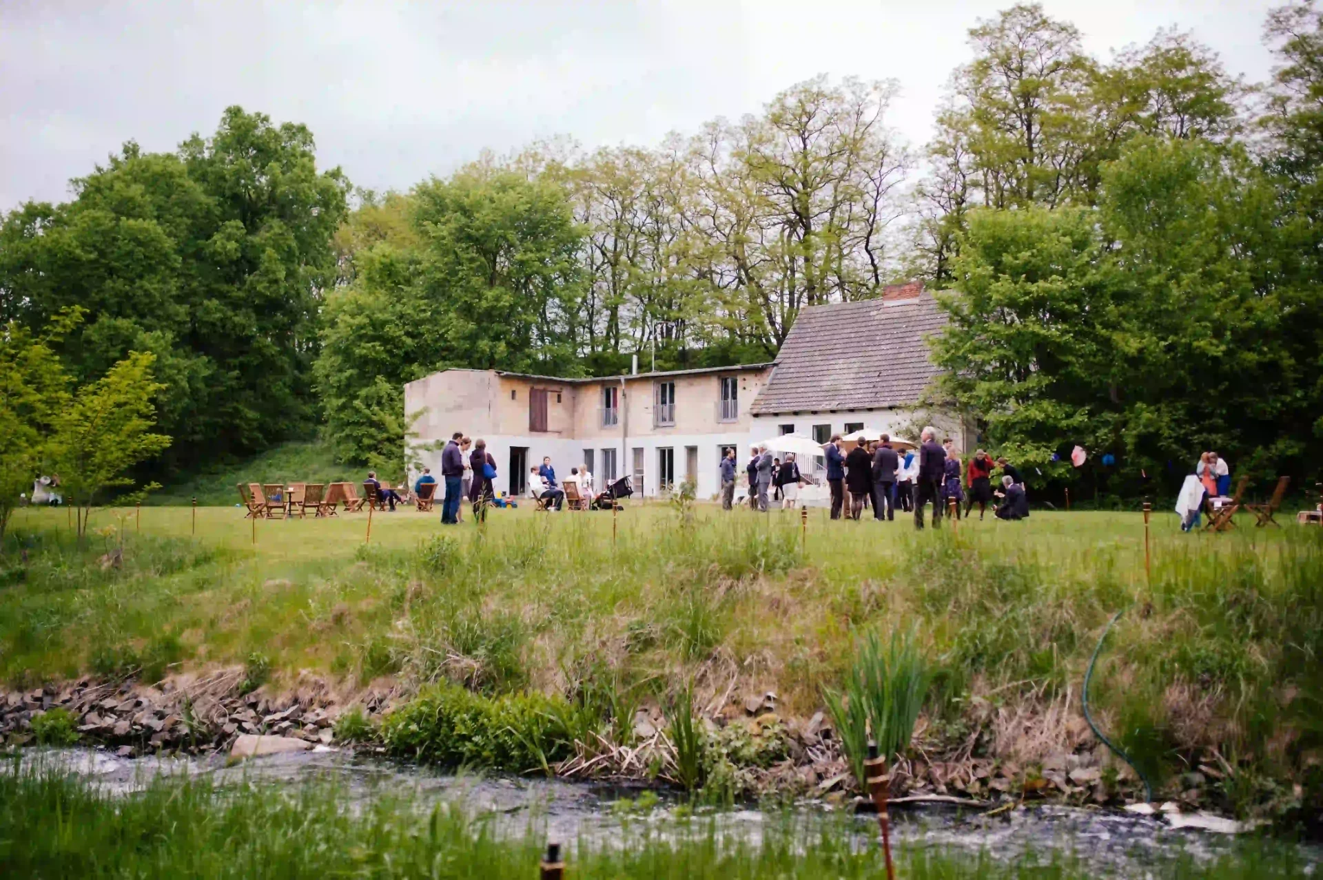 Exterior of a building beside the water, surrounded by trees and gardens