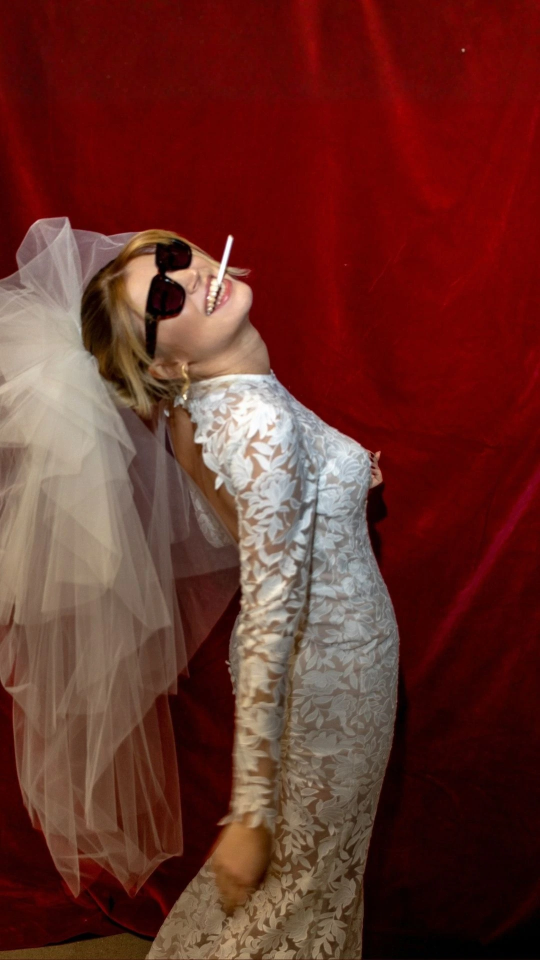 Bride in a lace wedding dress and sunglasses against a red backdrop