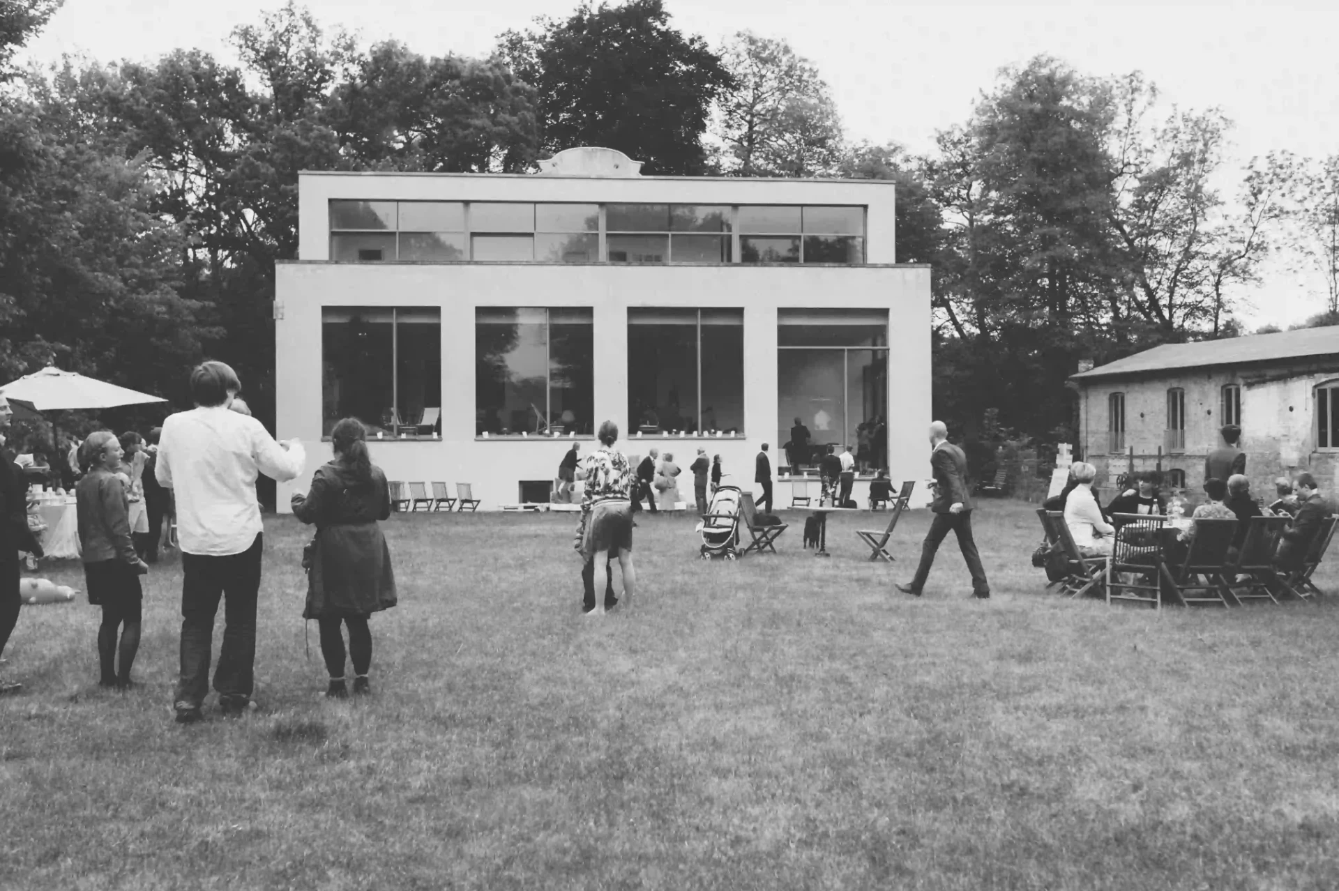 Black-and-white photograph of guests outside a modern building in a garden