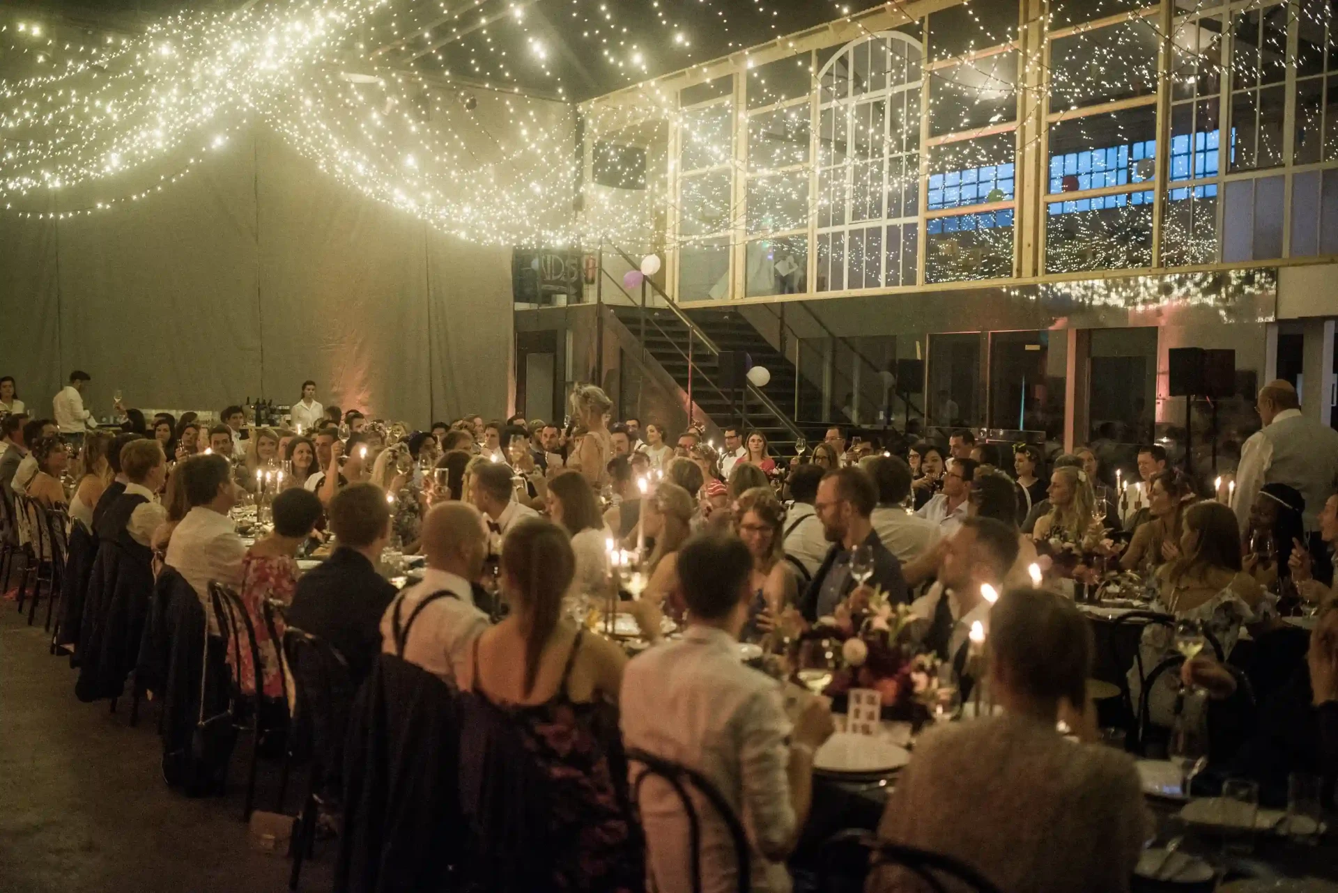 Wedding guests seated at a long table beneath string lights