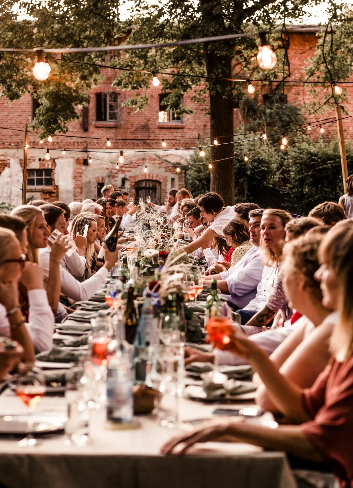 Outdoor wedding dinner at a long table beside a historic brick building