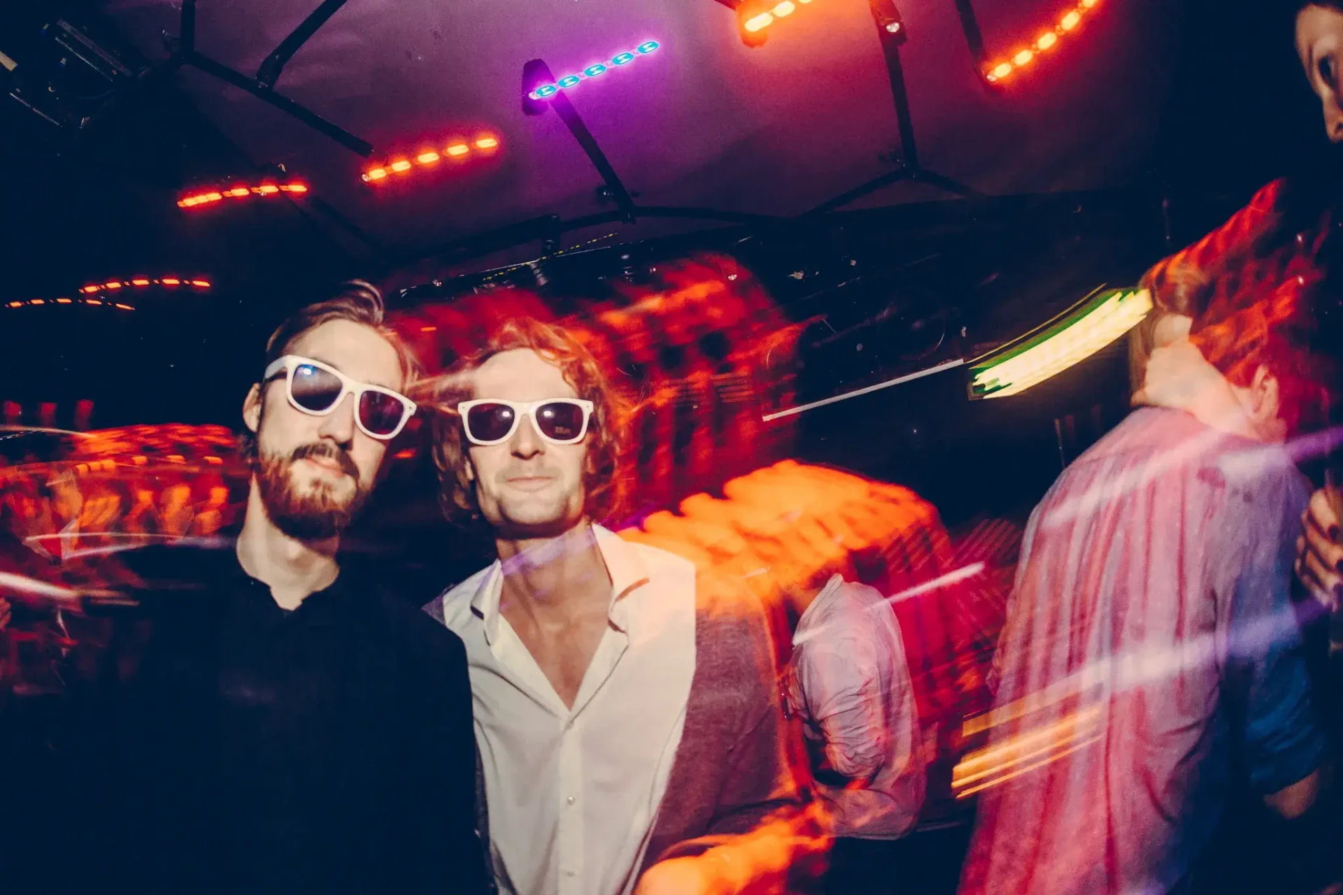 Two guests wearing sunglasses celebrating under colourful lights