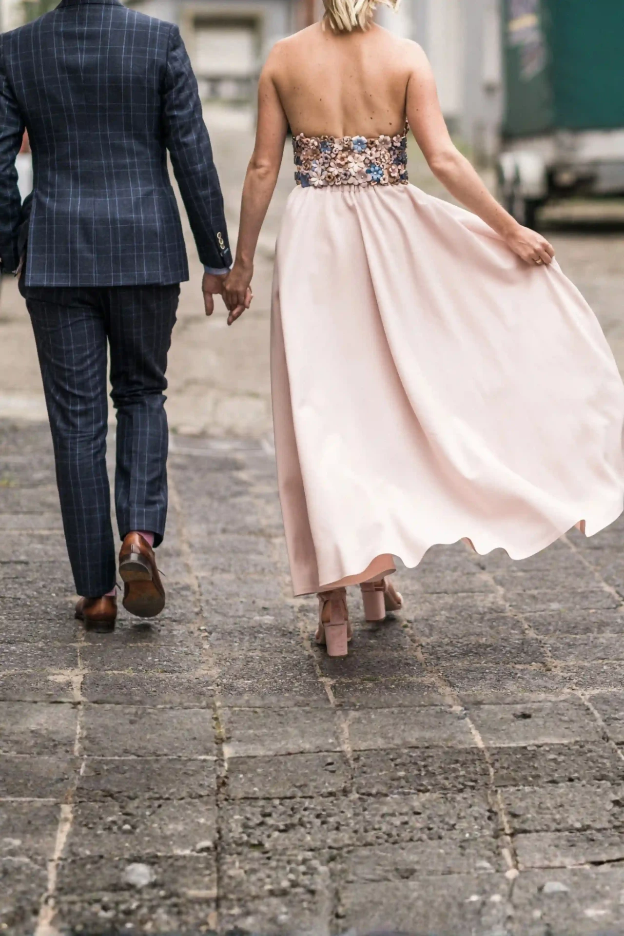 Bride and groom walking hand in hand along a cobblestone street, seen from behind