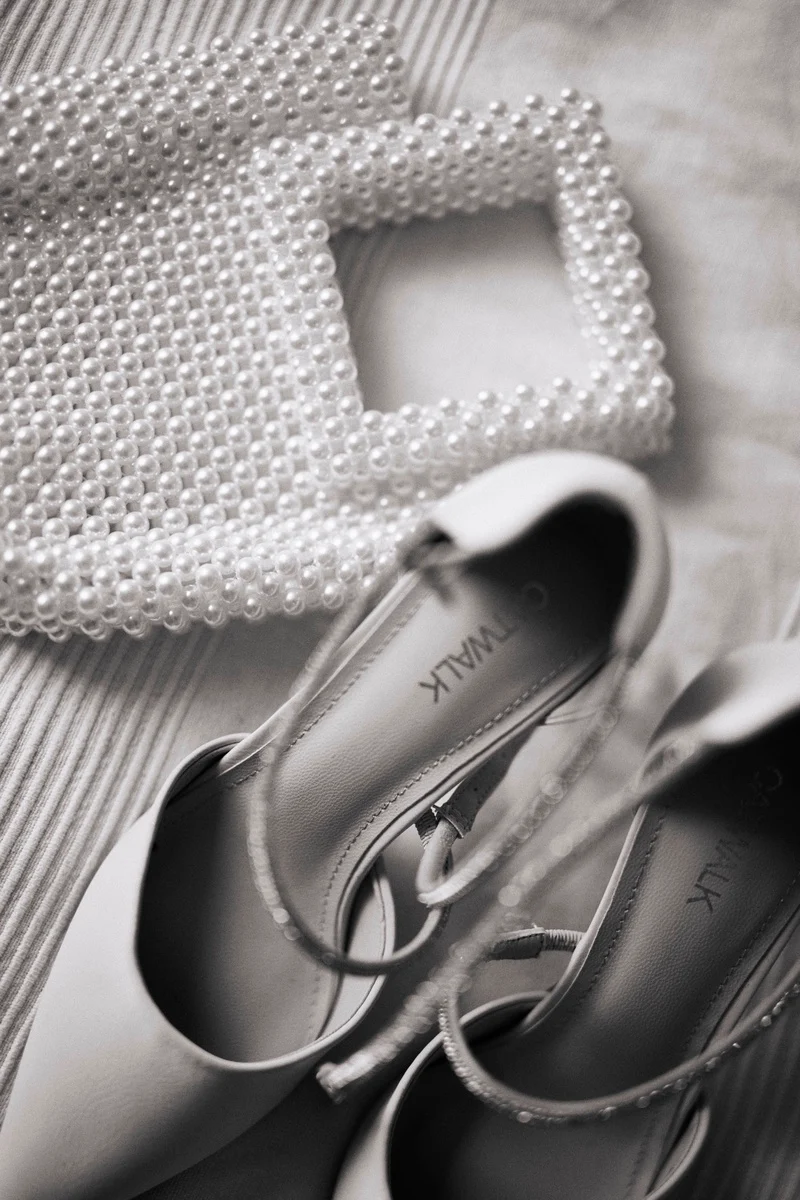 Detail of a pearl necklace beside a light-coloured shoe on textured fabric