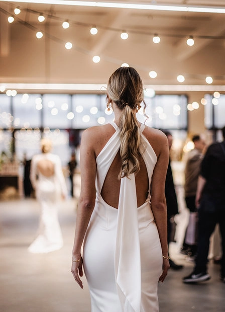 Bride in a white dress seen from behind in the exhibition space