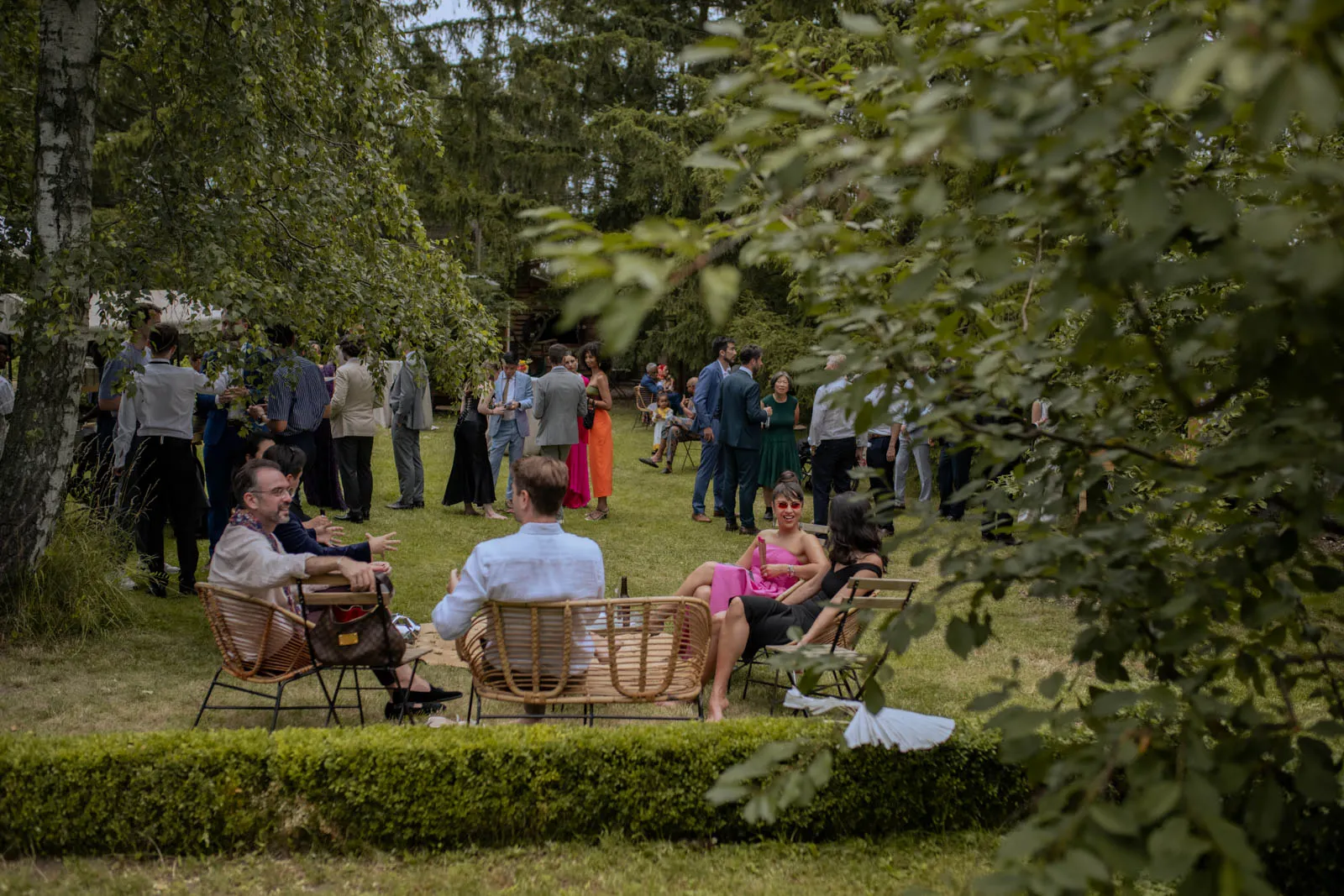Guests seated in a meadow among trees and garden furniture