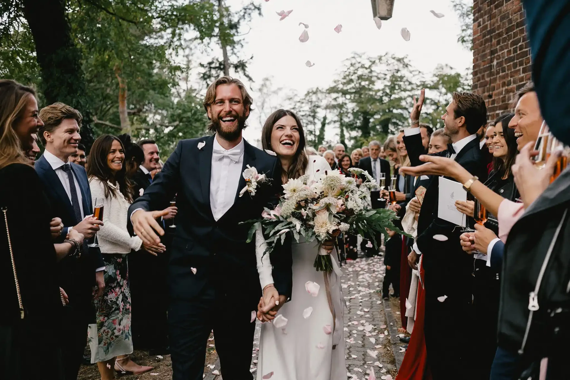 Laughing bride and groom with a bouquet surrounded by wedding guests