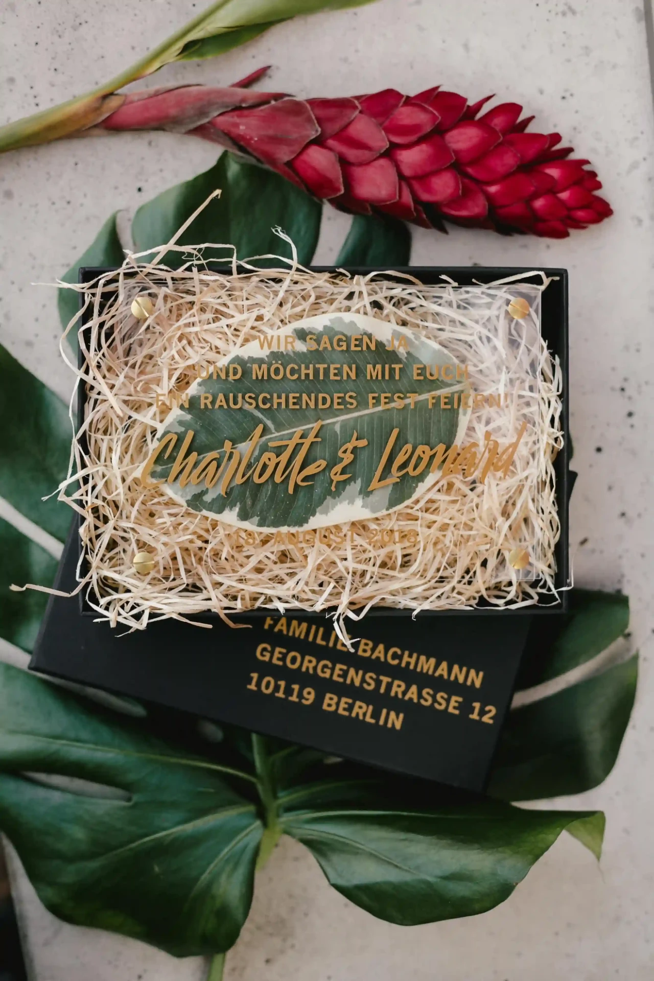 Dunkle Einladungskarte auf grünen Blättern mit roten Blüten