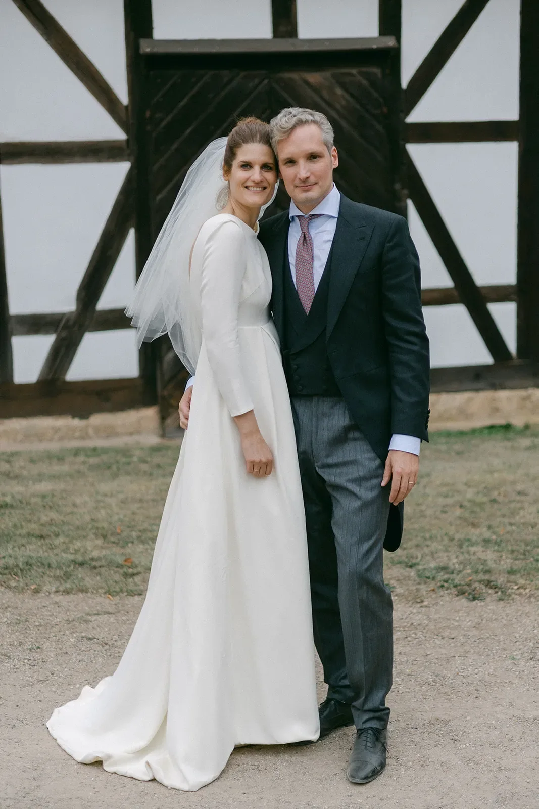 Wedding couple standing in front of a half-timbered building, with the bride wearing a long white dress