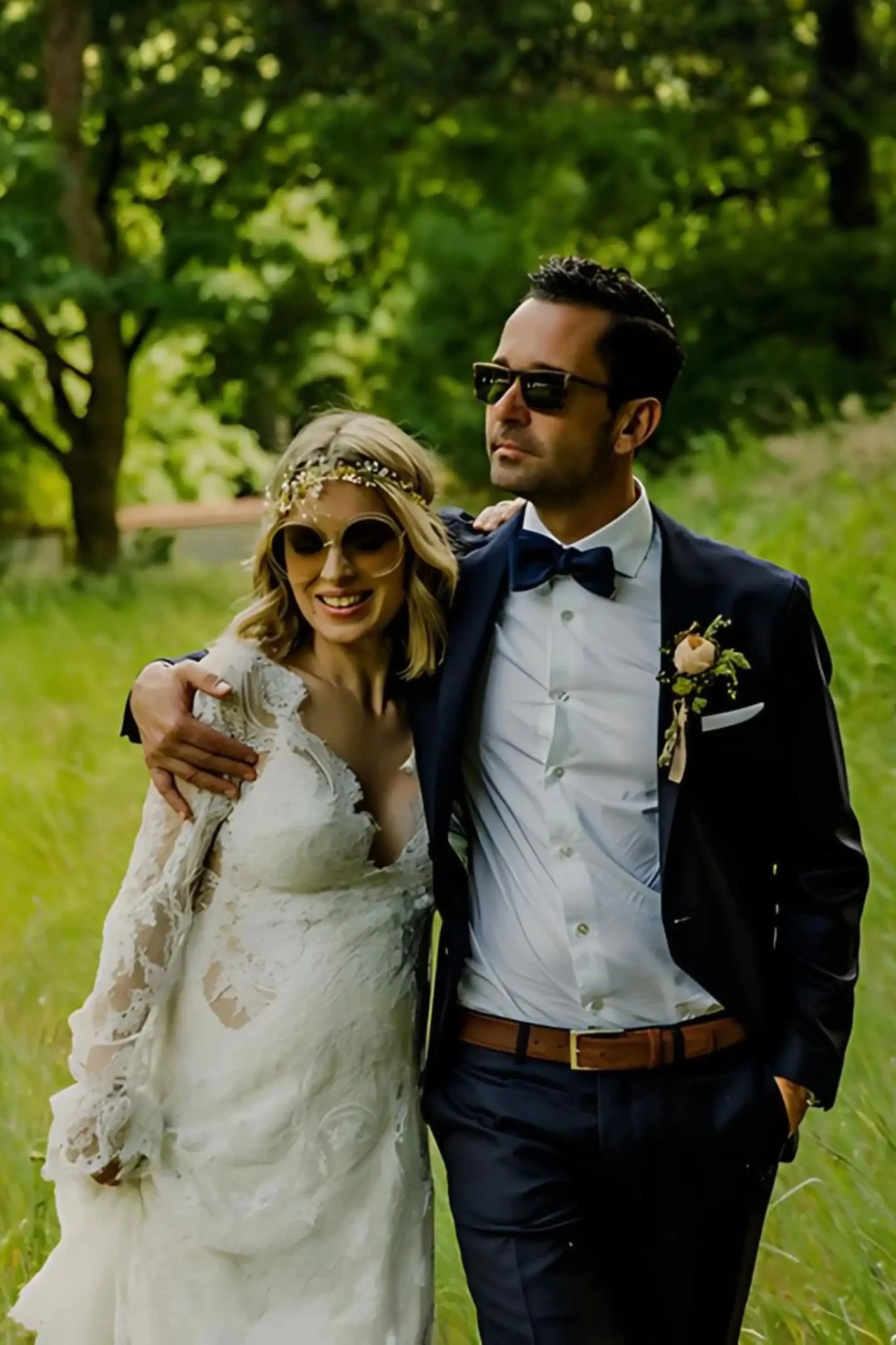 Bride and groom wearing sunglasses, standing close together in a leafy garden