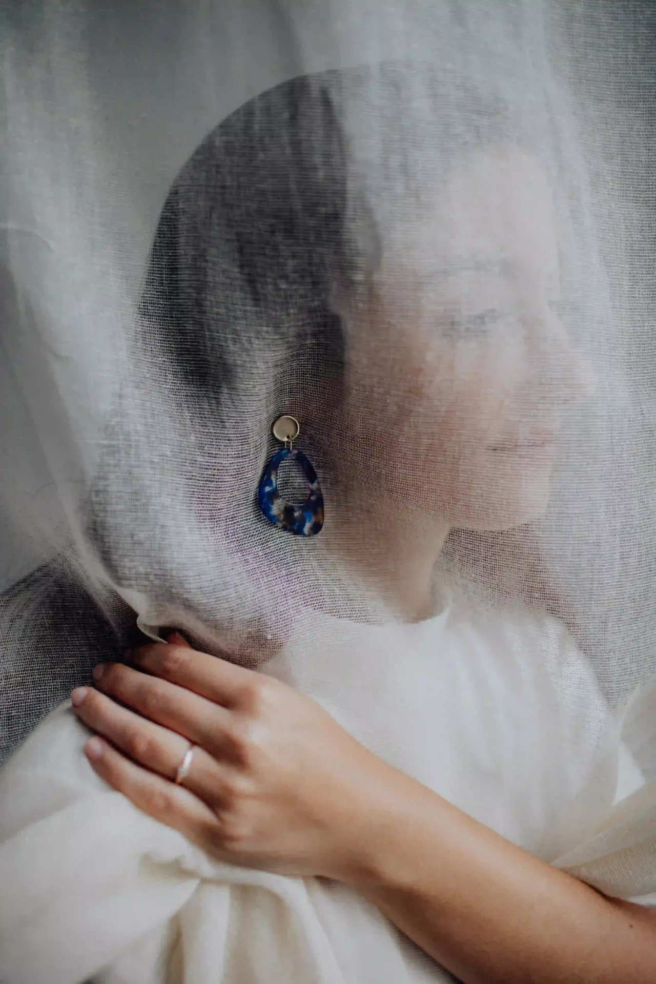 Bride wearing a veil in backlight, with one hand at her neck and veil