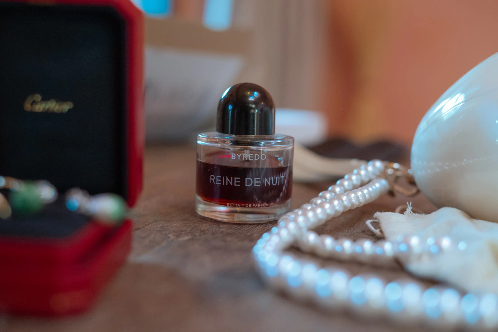Perfume bottle beside a pearl necklace and a white bridal accessory