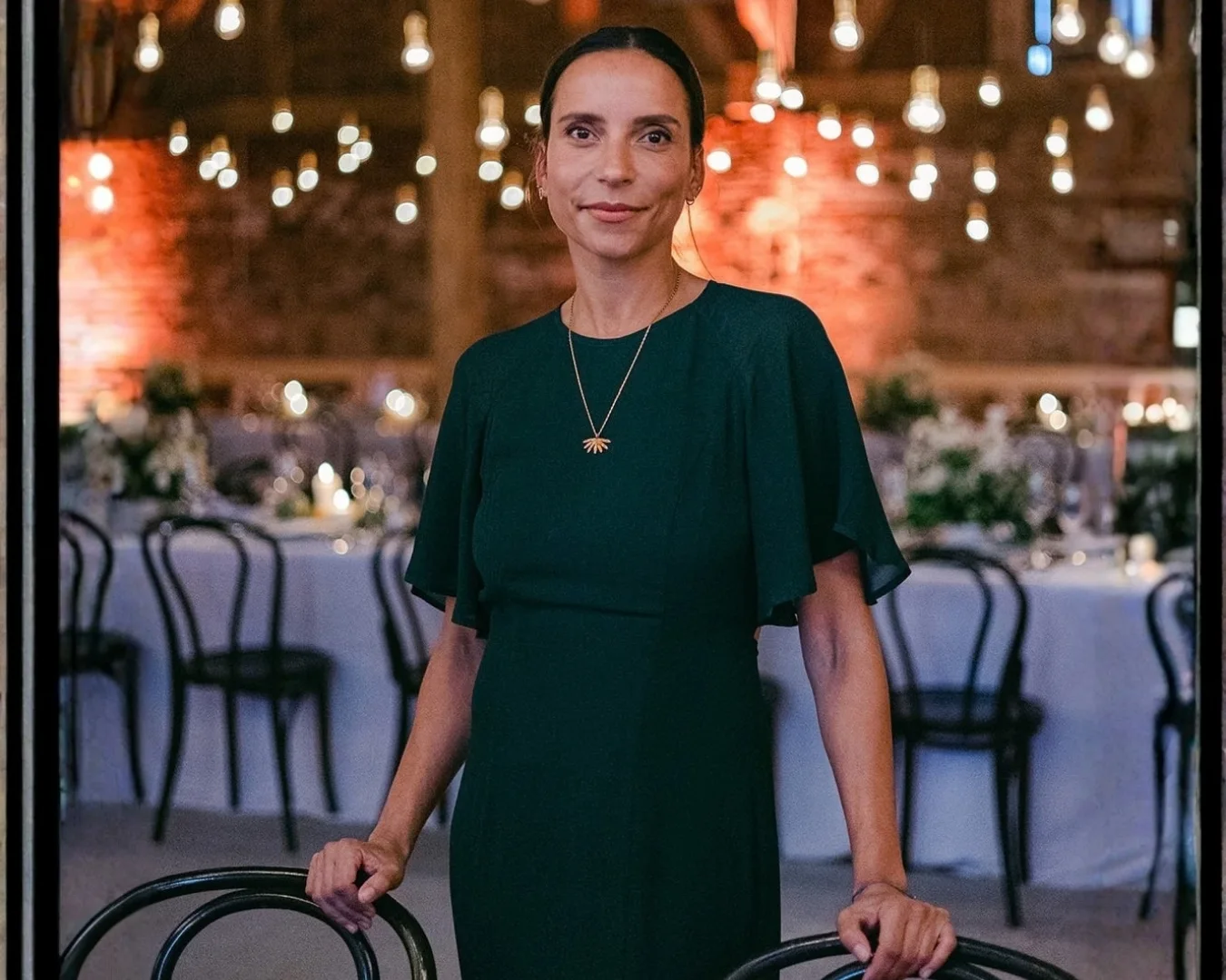 Woman in a dark green dress among dining tables at an evening event