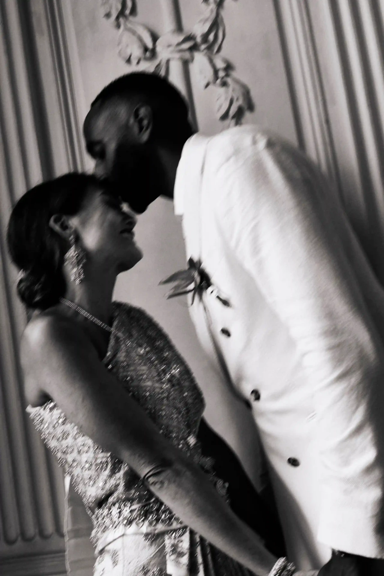 Bride and groom kissing in front of a curtain, black-and-white photograph
