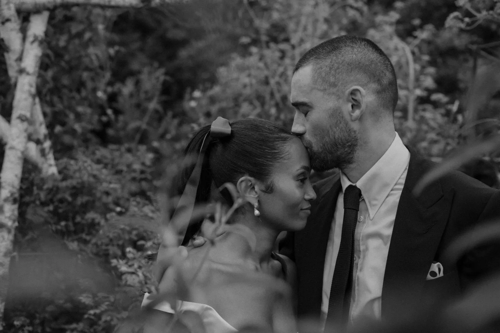 Black-and-white portrait of the groom kissing the bride on the forehead