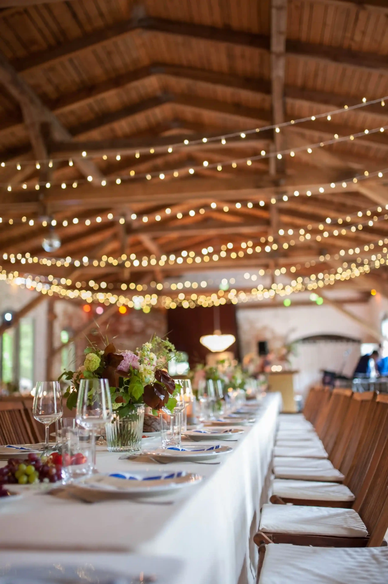 Long wedding table beneath wooden beams and string lights