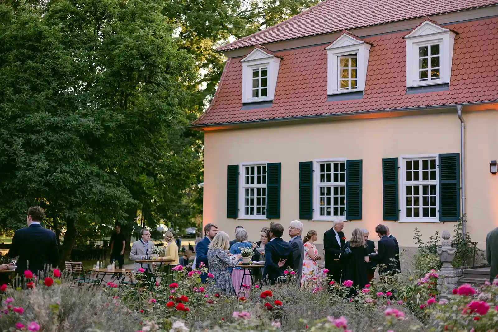 Wedding guests in front of a light-coloured country house with a red roof