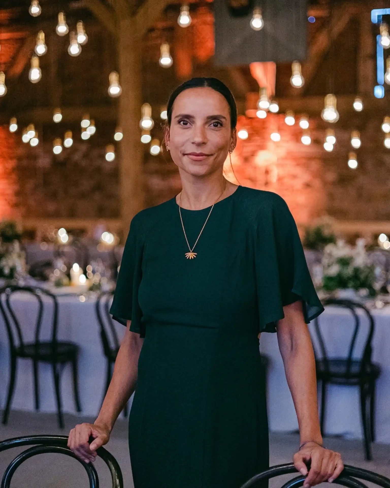 Woman in a dark green dress among dining tables at an evening event