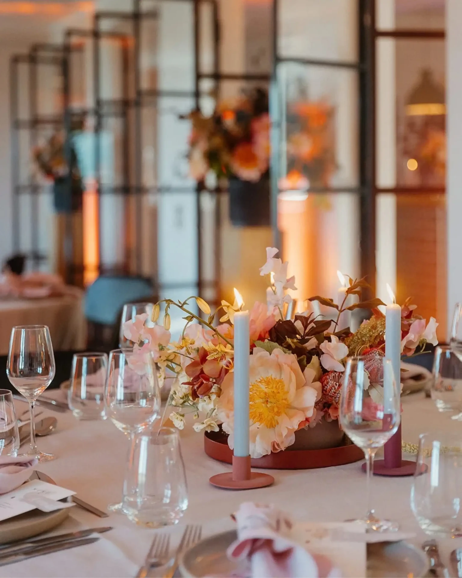 Modern minimalist wedding table setting with sculptural floral design, candles and elegant glassware