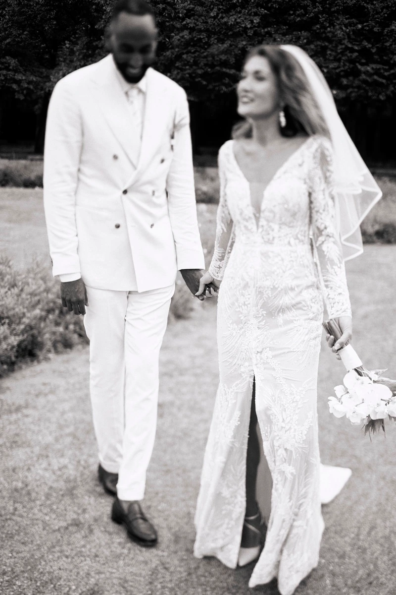 Bride and groom in white outfits walking together along a path