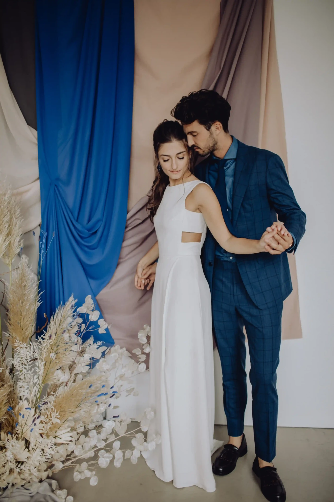 Wedding couple standing in front of blue curtains, the groom wearing a blue suit