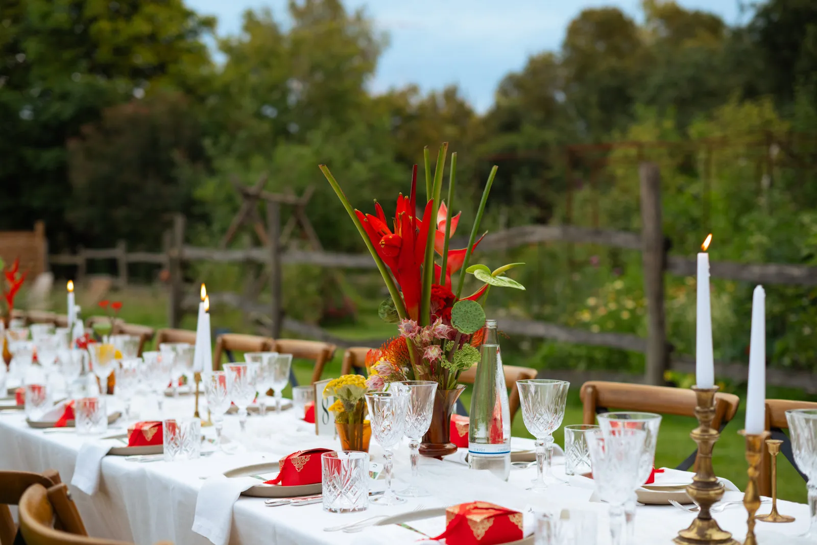 Garden wedding table set with candles and red floral arrangements