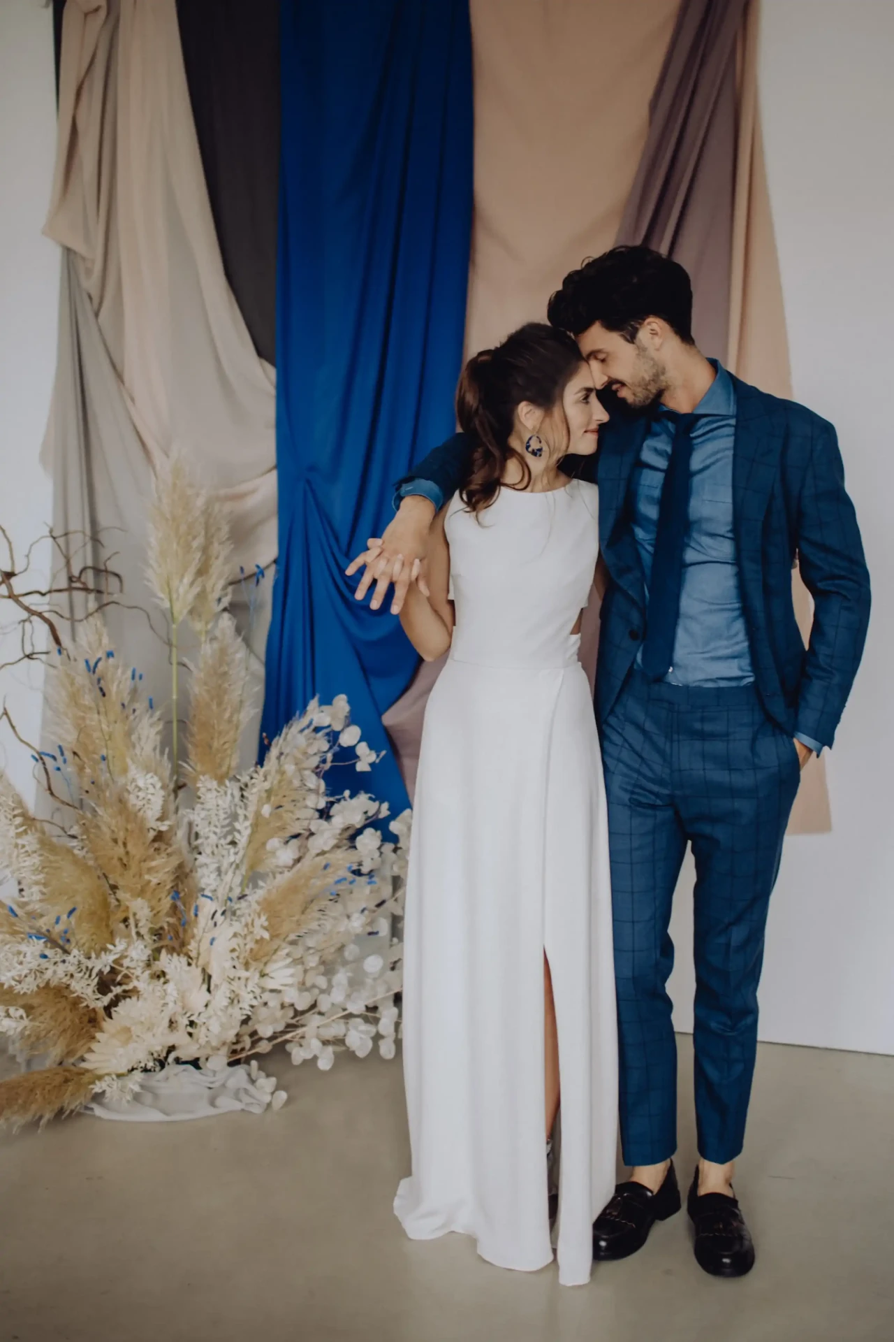 Wedding couple standing close together in front of blue curtains