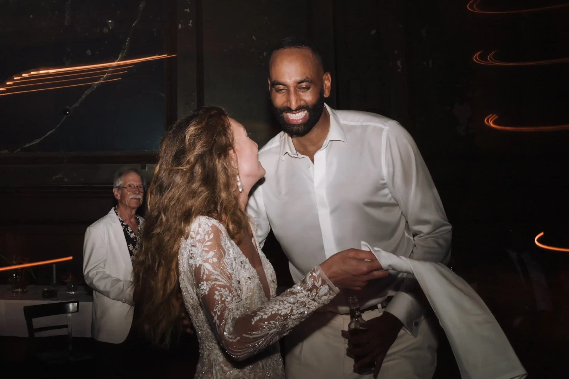 Bride and groom laughing and dancing at a celebration, the groom wearing a white shirt