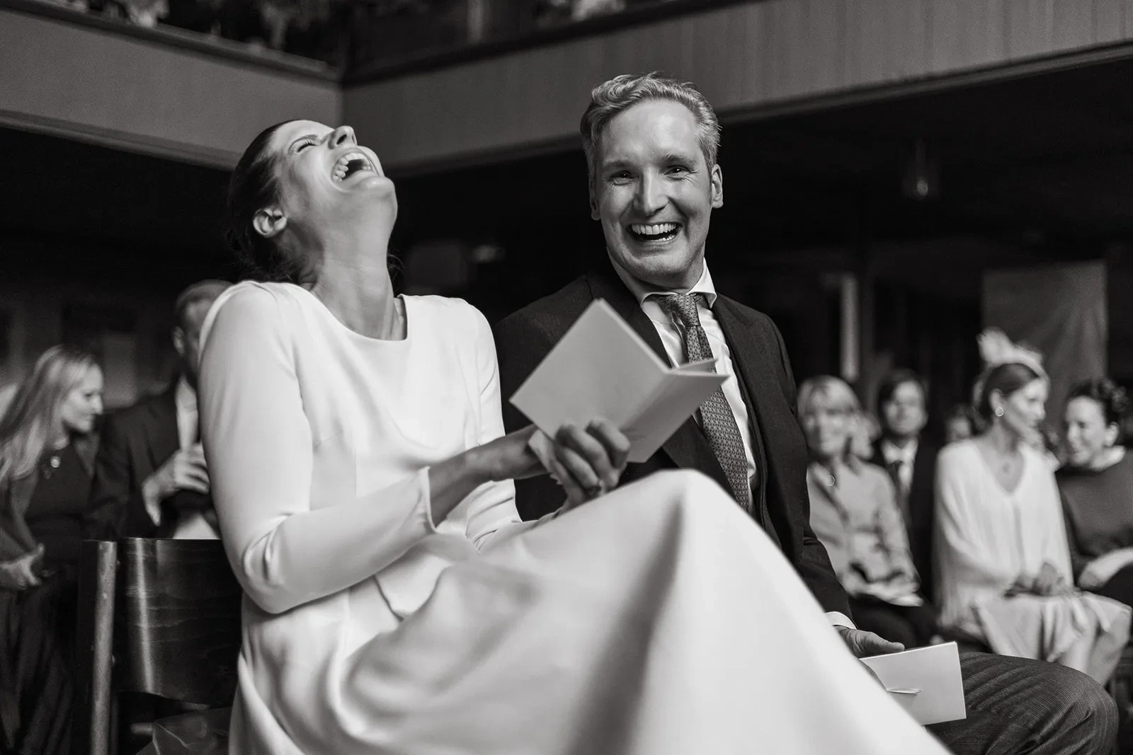 Bride laughing while seated beside a guest at the wedding celebration