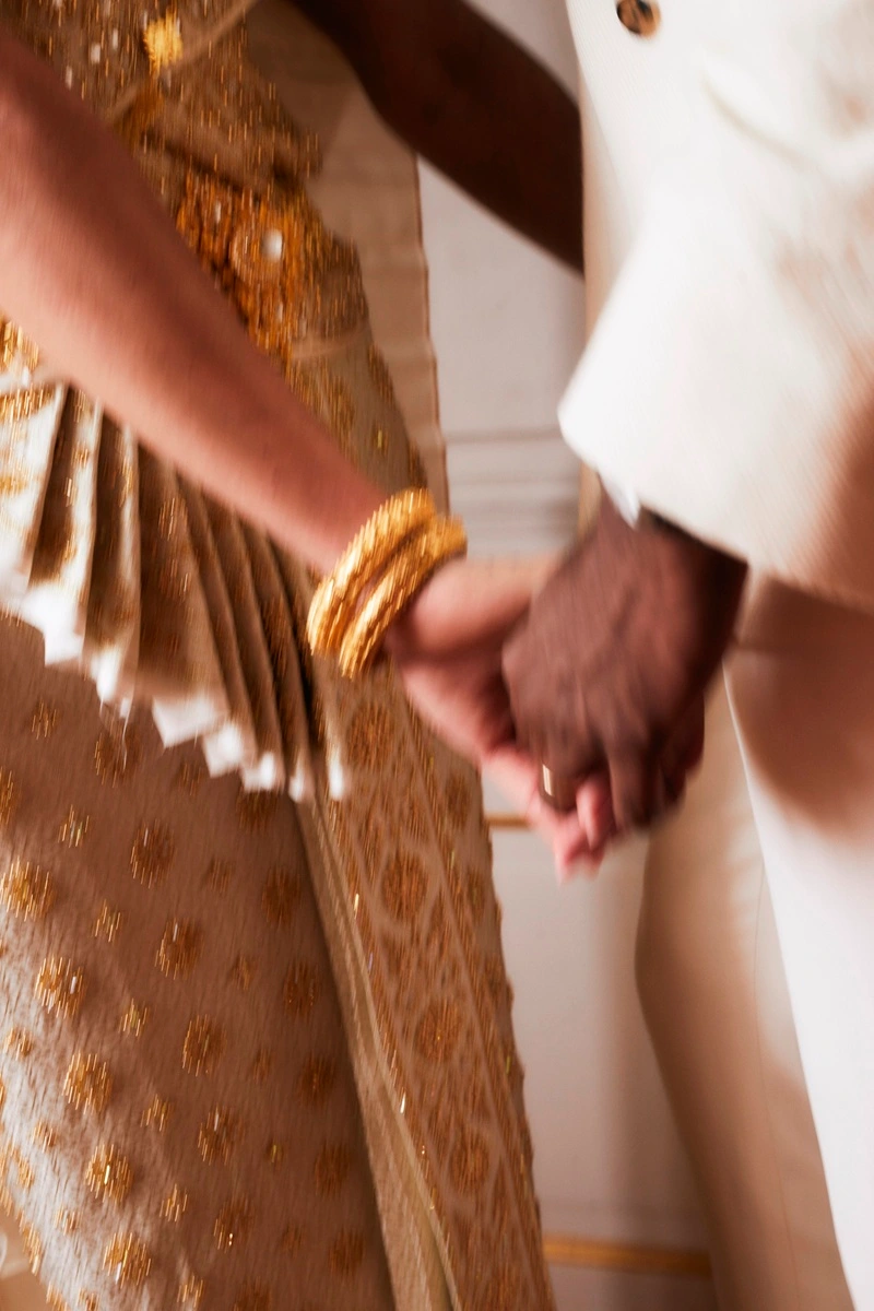 Bride and groom holding hands, detail of jewellery and clothing